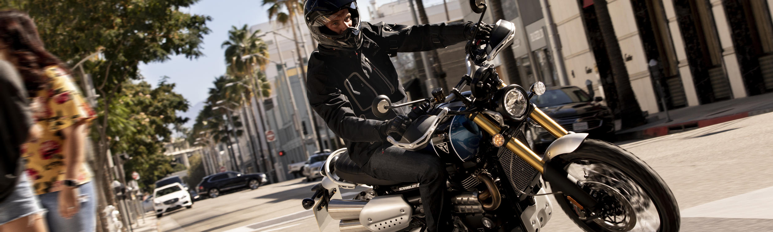 Motorcycle rider on Triumph bike rounding corner on city street.