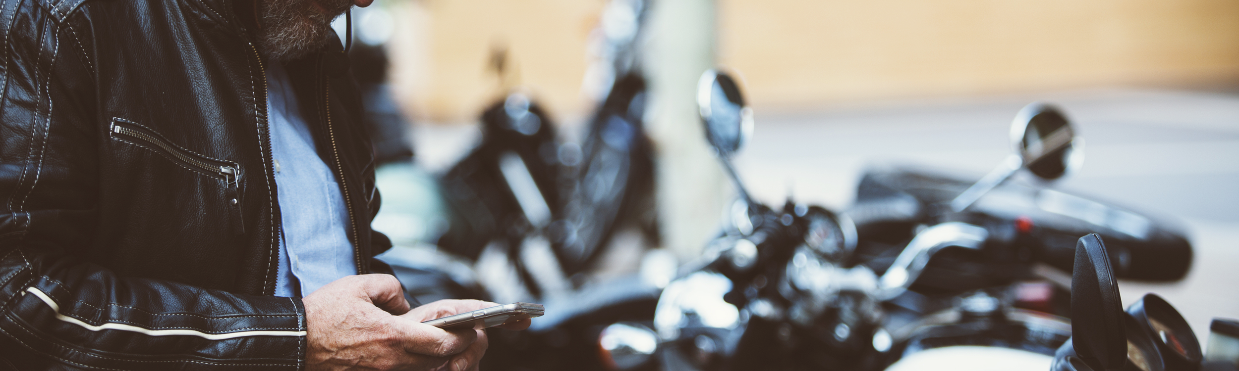 Motorcycle rider texting on his phone while standing by his bike.