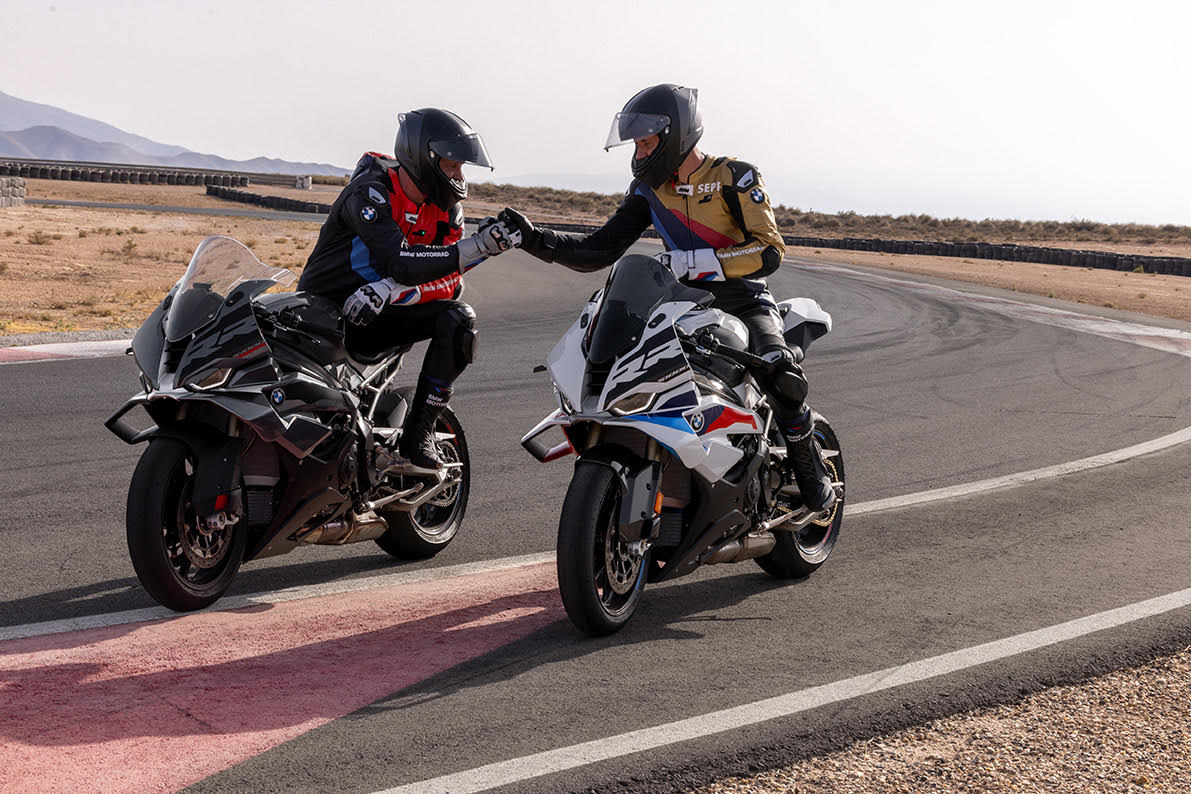 Two BMW Motorrad riders on BMW S 1000 RR sport motorcycles fist bump on a racetrack